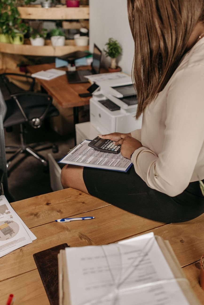Professional woman using calculator to review financial documents in a modern office setting.